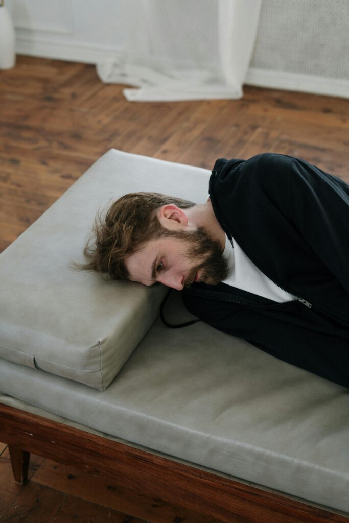 pexels-photo-4101155-4101155 A man lies on a couch indoors, appearing deep in thought or contemplative mood.