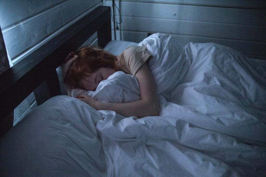pexels-photo-935777-935777 A woman sleeping peacefully in a cozy bedroom, enveloped by soft white sheets, under the gentle glow of night lighting.