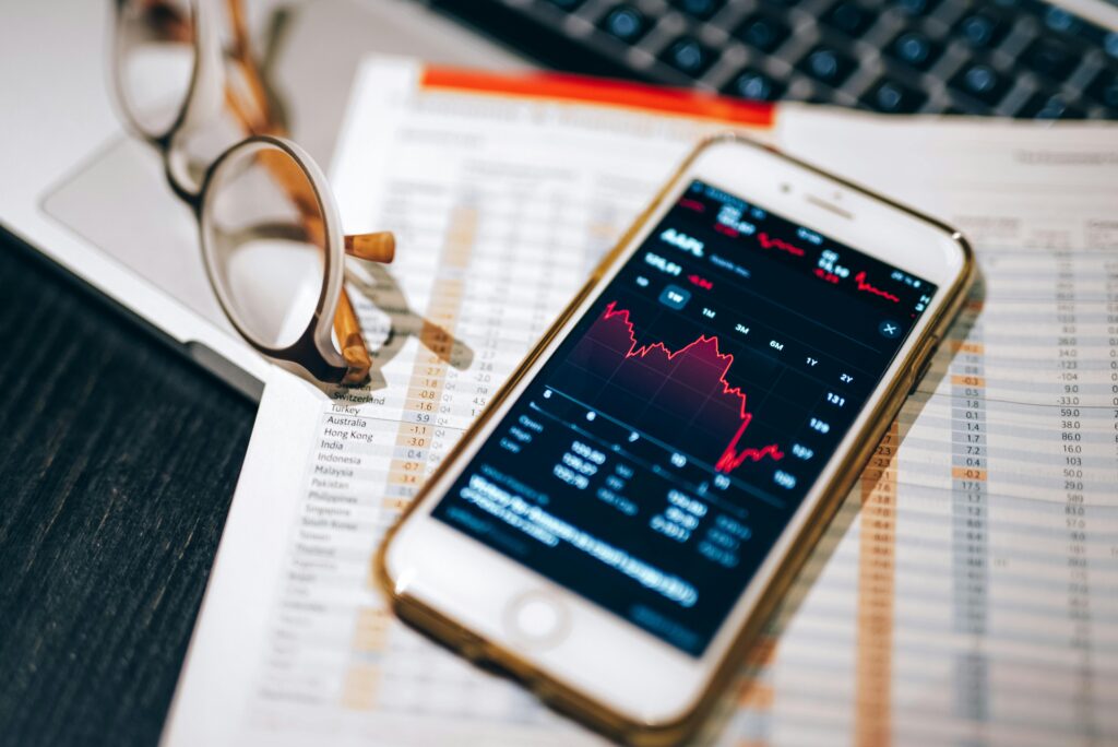 pexels-photo-7873553-7873553 Smartphone displaying stock market chart on a financial spreadsheet with eyeglasses.